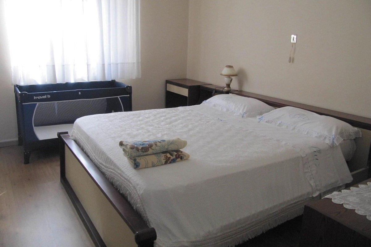 A bedroom with a bed, a bedside table, a lamp, and a window with curtains.
