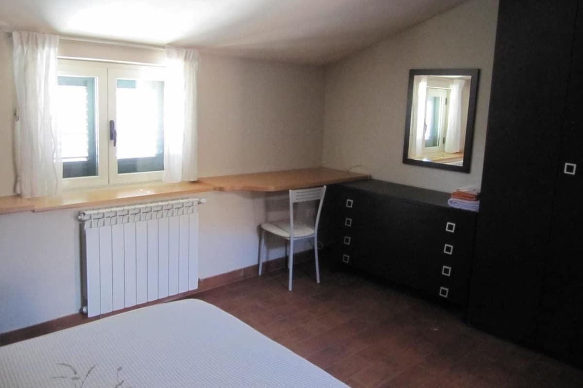 A small, sparsely furnished room with a radiator, a chair, a desk, and a mirror on the wall.