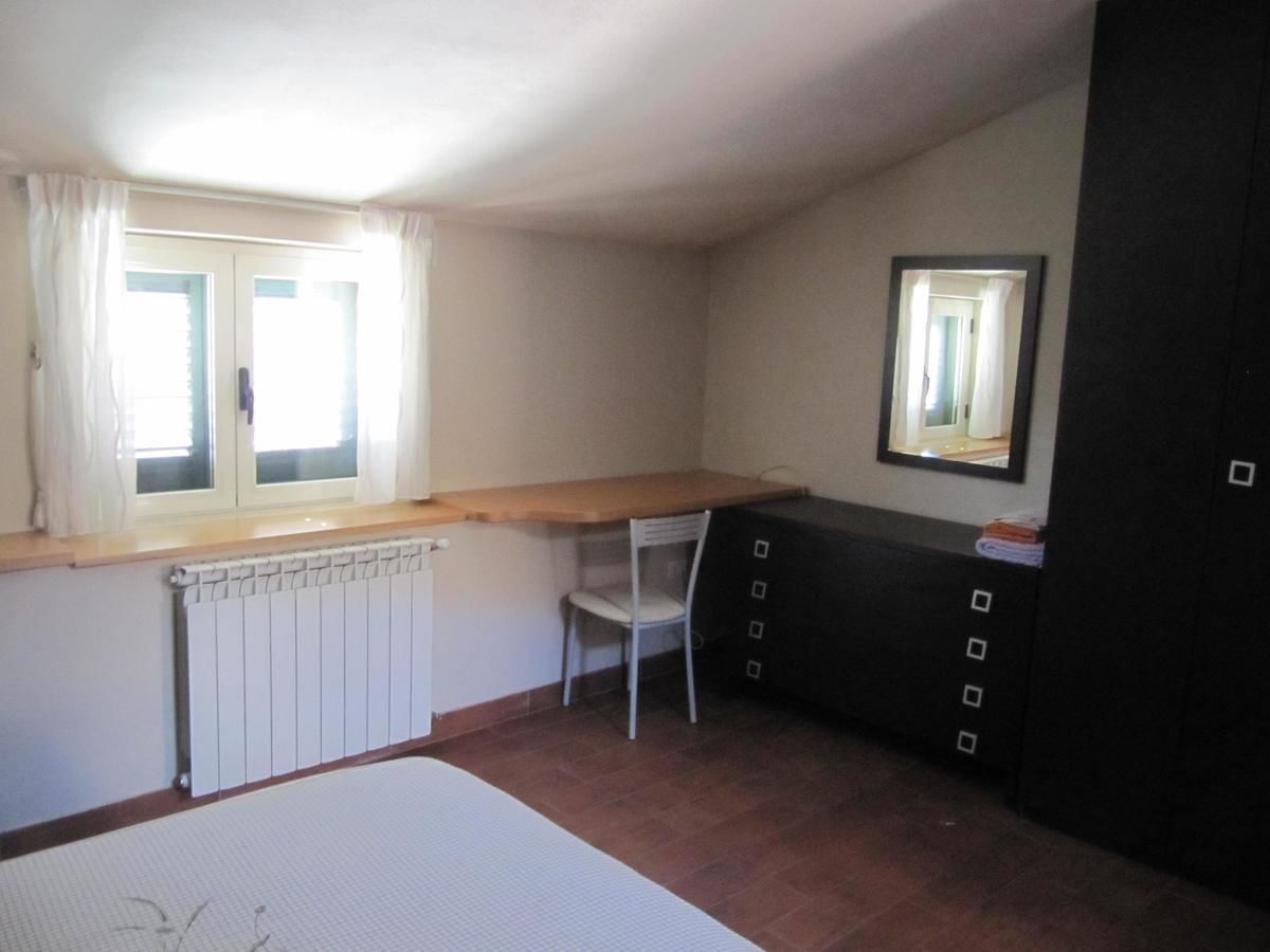 A small room with a radiator, a window with curtains, a chair, a desk with a mirror, and a cabinet.