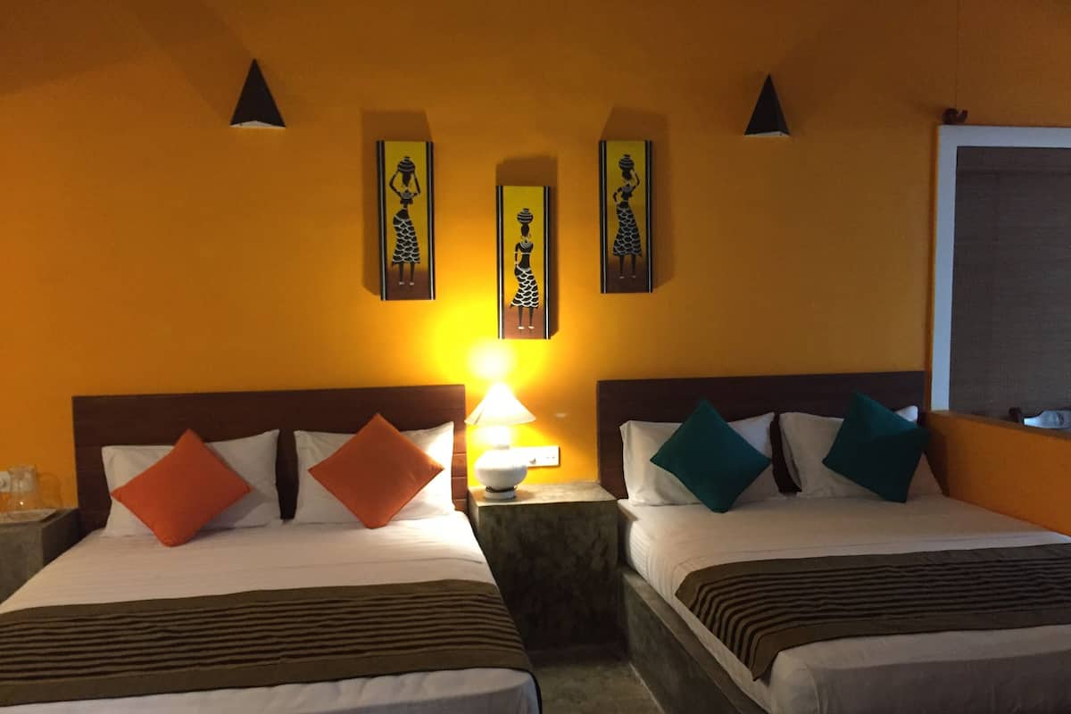 Habitación de hotel con dos camas, cada una con cabecero de madera, ropa de cama blanca y varios cojines. Se observan obras de arte colgadas en la pared sobre las camas y una mesita de noche con lámpara entre ellas.