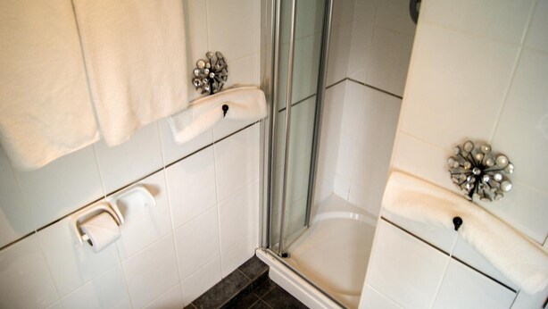 Un baño con cabina de ducha de vidrio, azulejos blancos y un perchero para toallas.