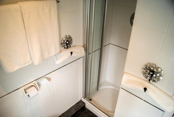 A bathroom with a glass shower enclosure, white tiles, and a towel rack. - THE Cumberland (Bournemouth)