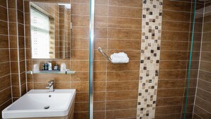 Un baño con lavamanos blanco, un espejo, ducha con puerta de cristal y un perchero para toallas.