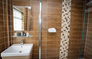 A bathroom with a white sink, a mirror, a shower with a glass door, and a towel rack. - THE Cumberland (Bournemouth)