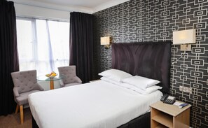 A hotel room with a bed, two armchairs, a small table with fruit, and a bedside telephone. - THE Cumberland (Bournemouth)
