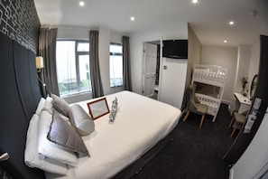 A hotel room with a large bed, a desk with a chair, a crib, and a TV on the wall. - THE Cumberland (Bournemouth)