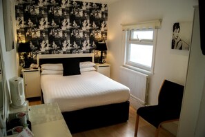 A neatly arranged bedroom with a bed, bedside tables, a chair, a window, and a wall with a patterned wallpaper. - THE Cumberland (Bournemouth)