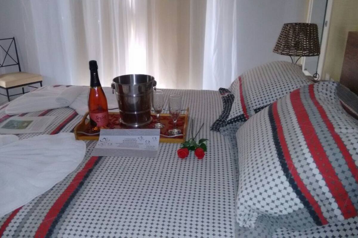 Une chambre d’hôtel avec un lit, une chaise, une table sur laquelle se trouvent une bouteille, des verres et un menu.