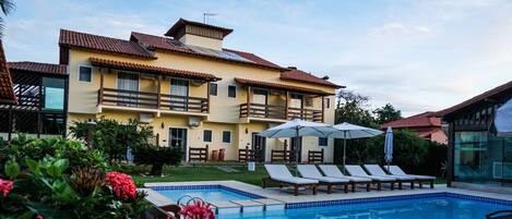 A hotel with a swimming pool, sun loungers, and a garden area.