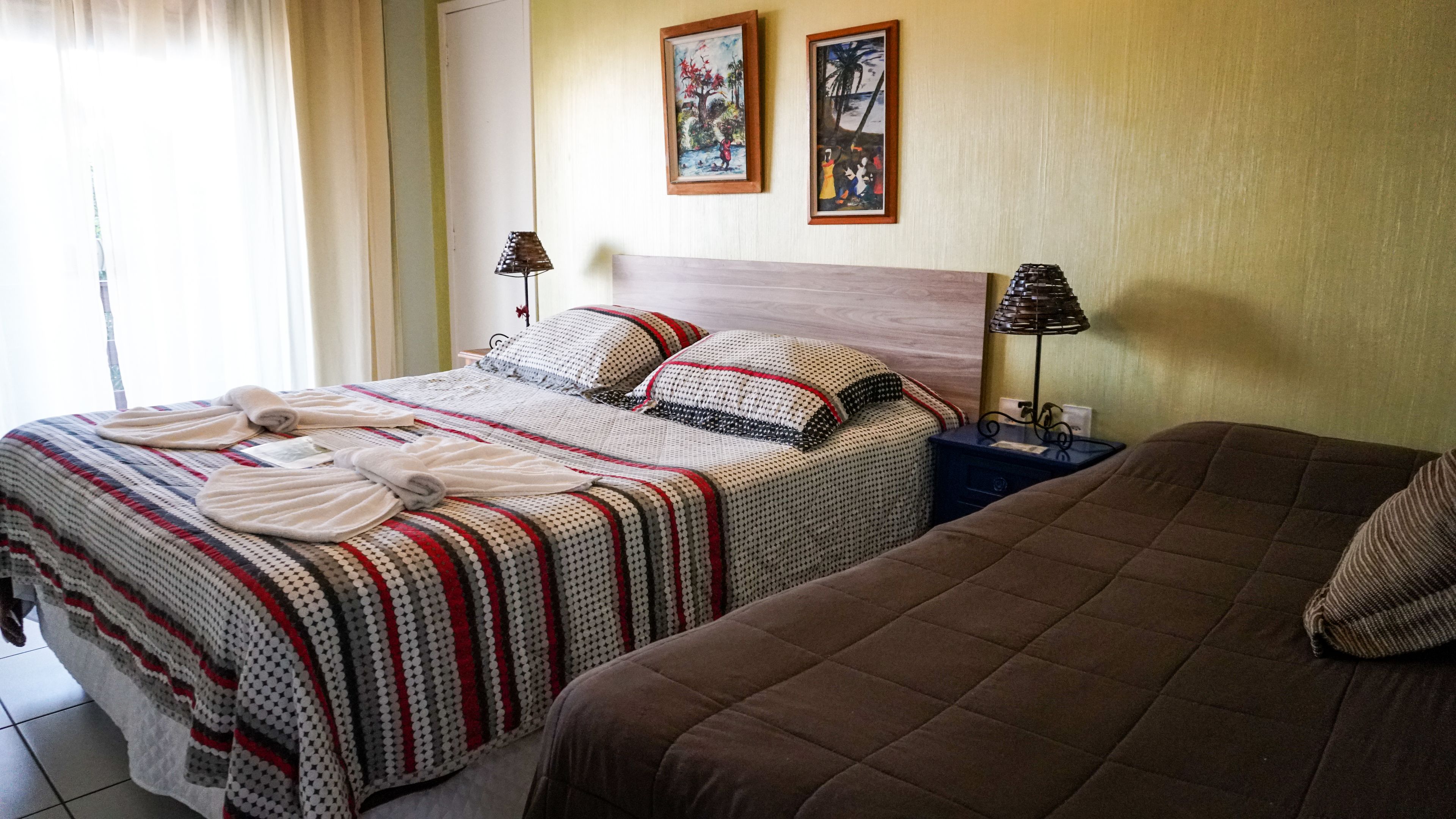 Quarto de hotel com duas camas, uma mesa de cabeceira com abajur e duas fotos emolduradas na parede.