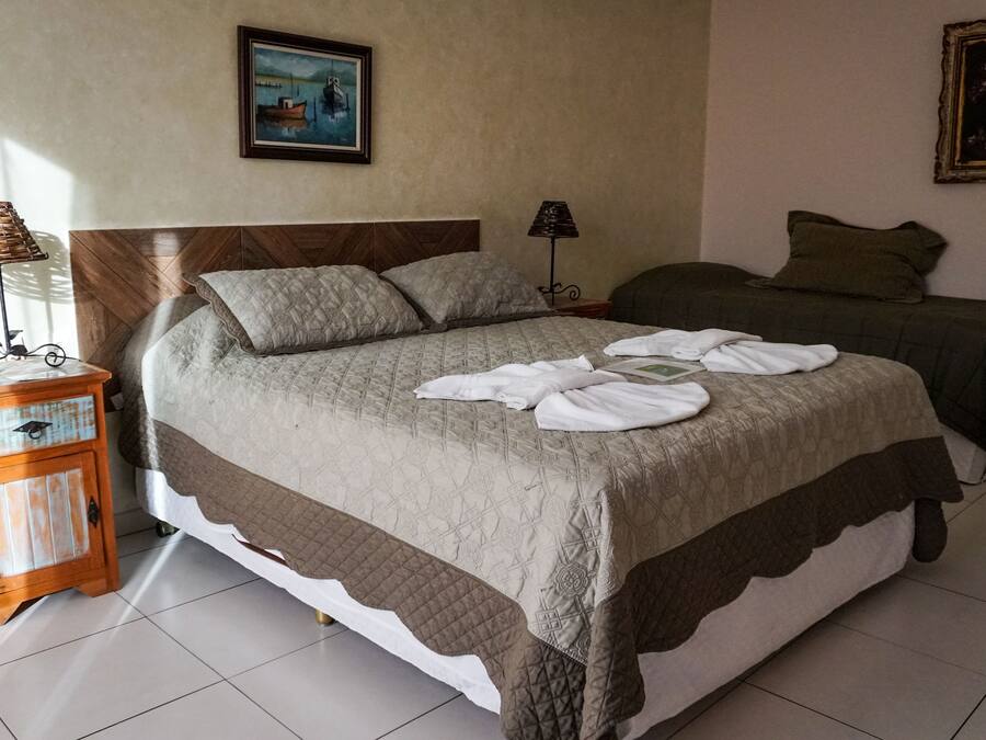 A double bed with a quilted bedspread, a nightstand with a lamp, and two paintings on the walls.