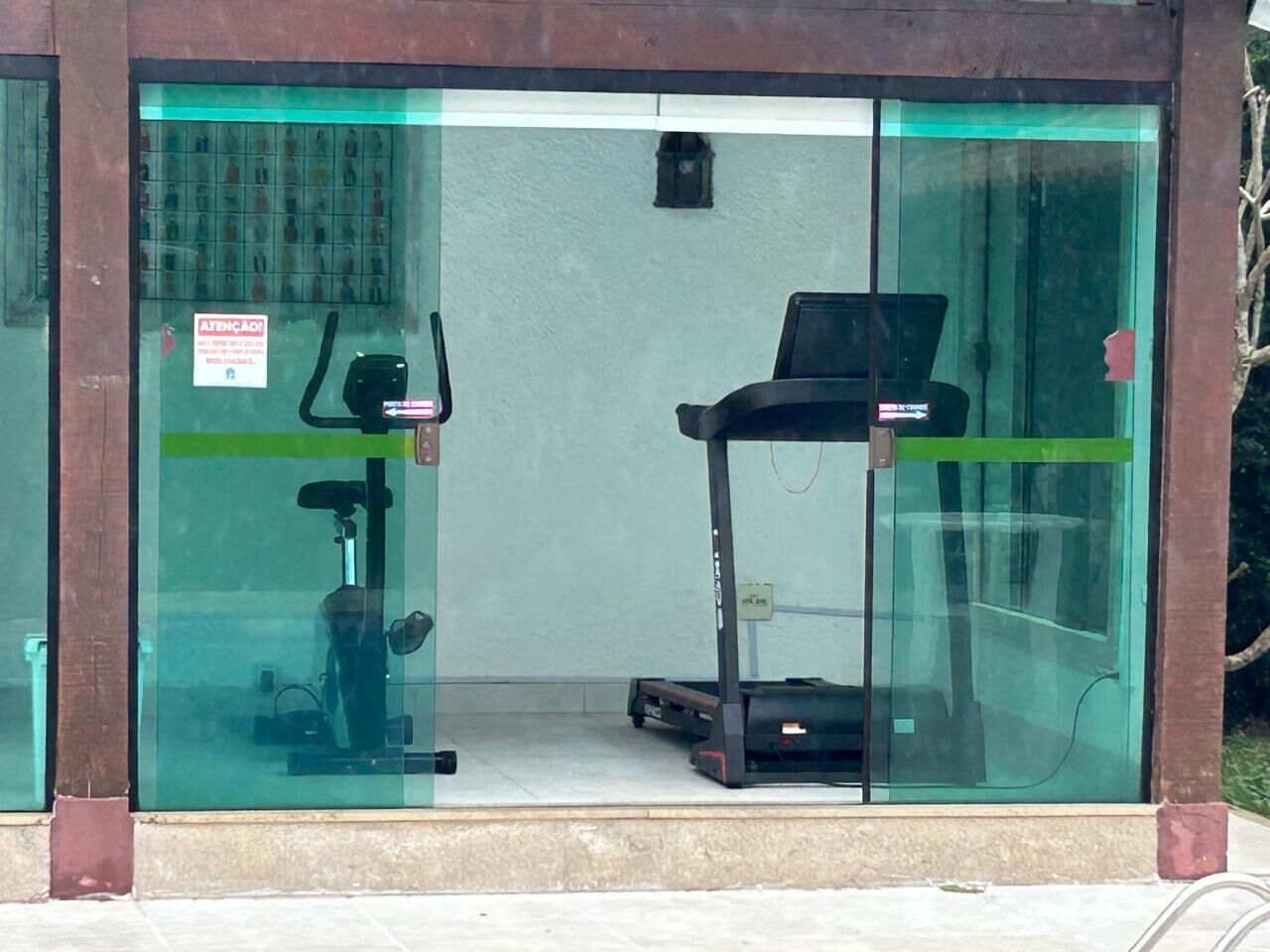 A fitness center with a treadmill and stationary bikes, enclosed by glass walls with a green stripe.