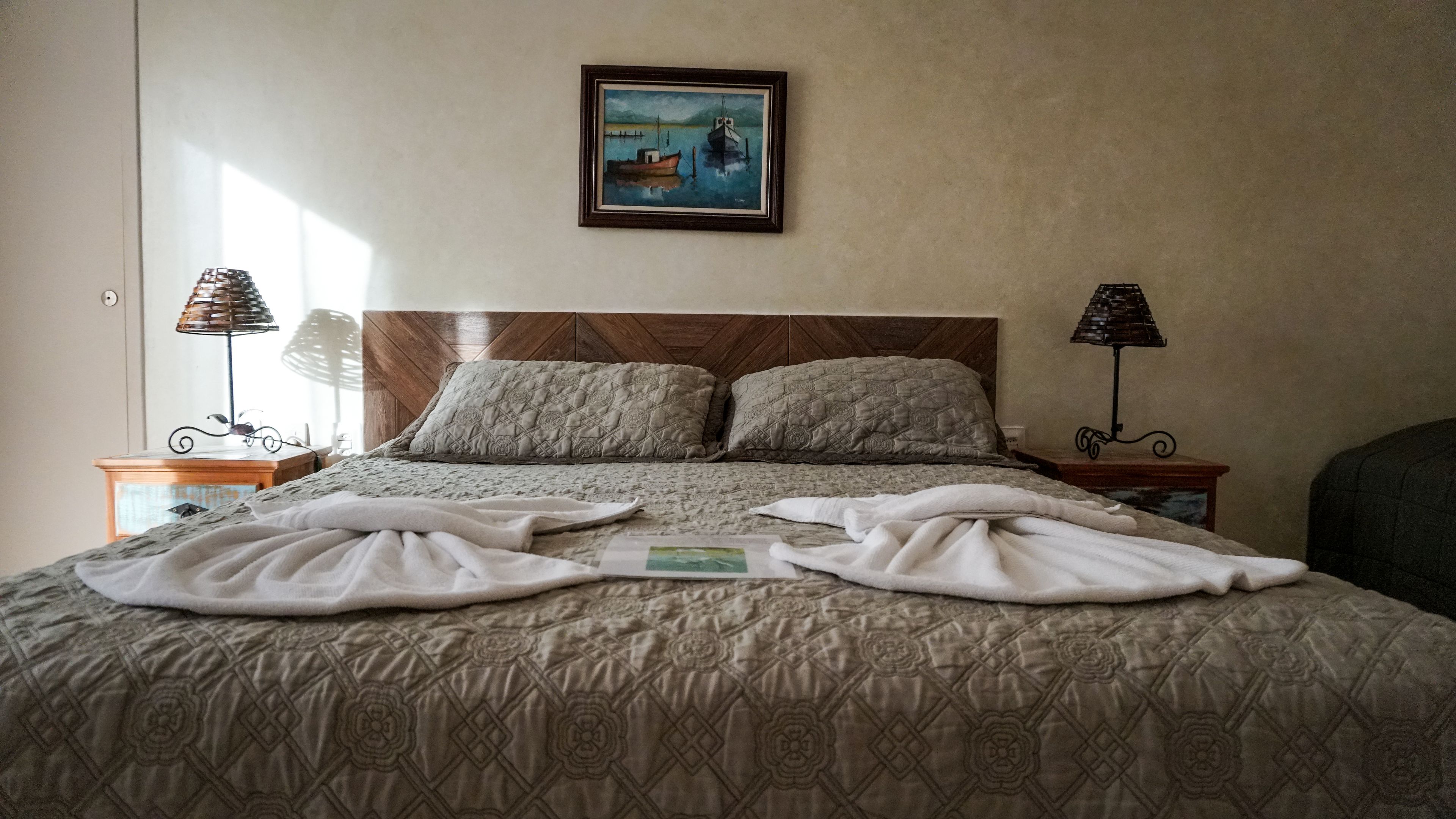 A neatly made bed with a patterned bedspread and pillows, two bedside lamps, and a framed painting on the wall.