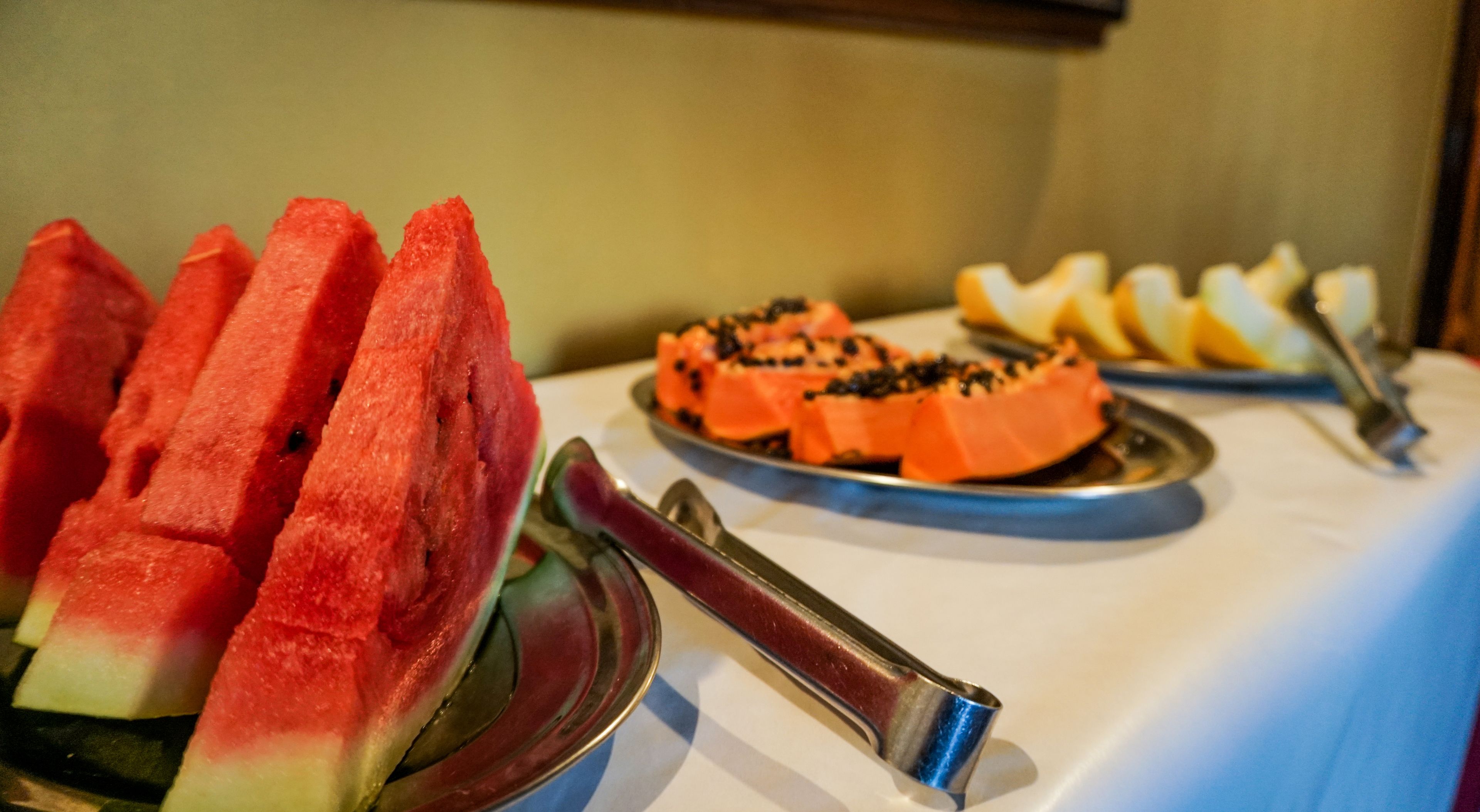 Une table de buffet avec des tranches de pastèque et d’autres fruits.