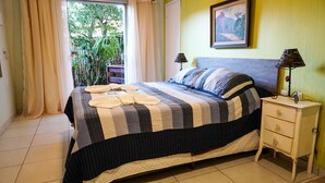 A neatly made bed with striped bedding, a bedside lamp, and a nightstand with drawers. - Pousada das Garças de Saquarema (Saquarema)