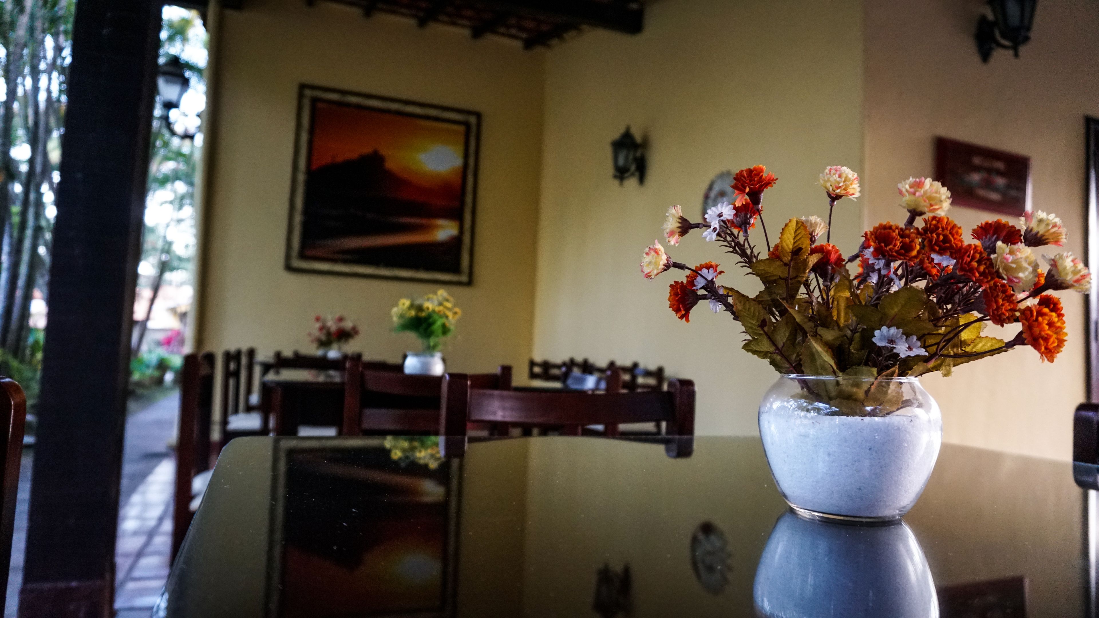 A dining area with a table and chairs, a vase of flowers, and a painting on the wall.