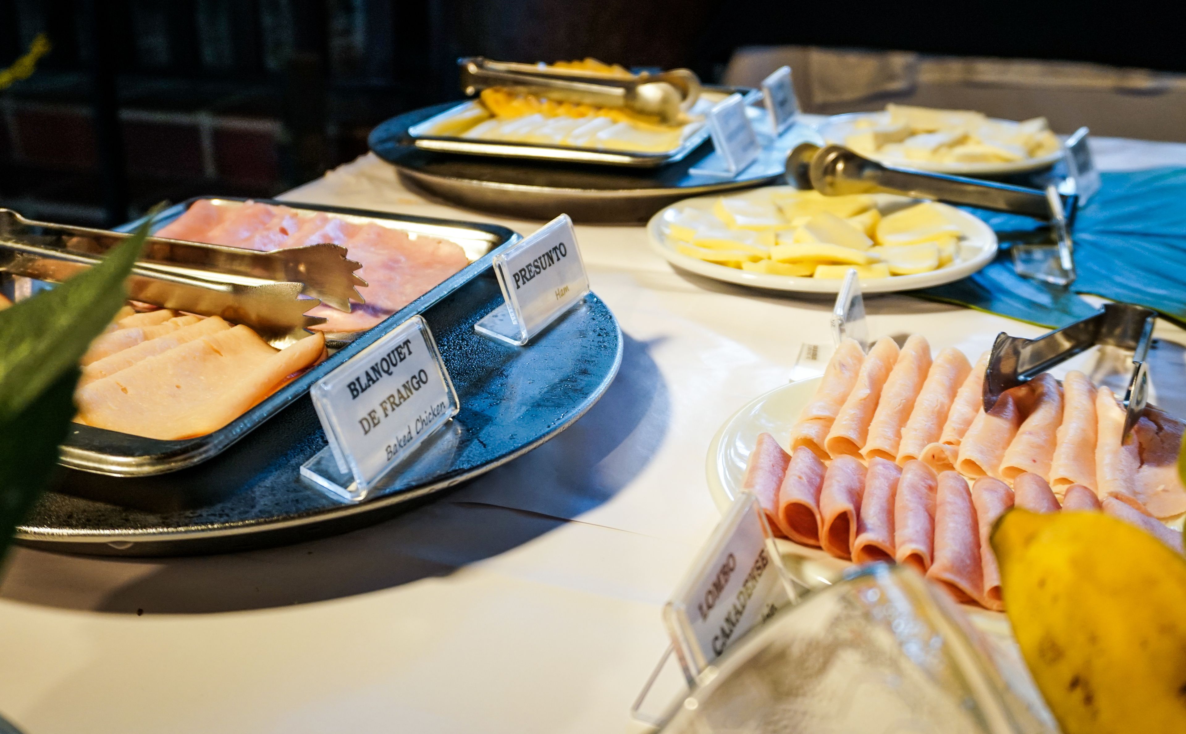 Une table de buffet proposant divers plats, notamment du jambon, du poulet rôti et du fromage.