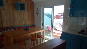 Una mesa de madera con taburetes, un armario azul y vistas a través de un ventanal.