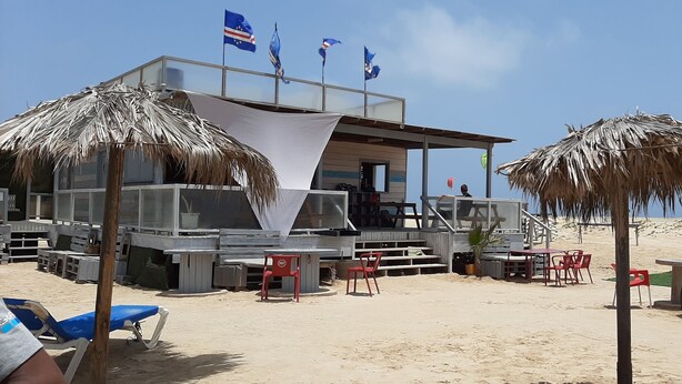 Un restaurante frente al mar con terraza, una zona cubierta y banderas.