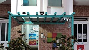 Fachada de edificio de piedra, toldo verde y plantas en macetas.