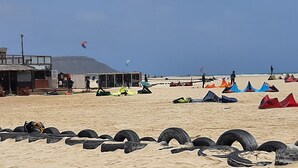 Una playa con tiendas de campaña y neumáticos en primer plano, un edificio con un cartel que dice
