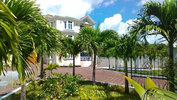A building with a white facade and multiple windows, surrounded by palm trees and a brick pathway. - Luxor Residence Guest House (Belle Mare)