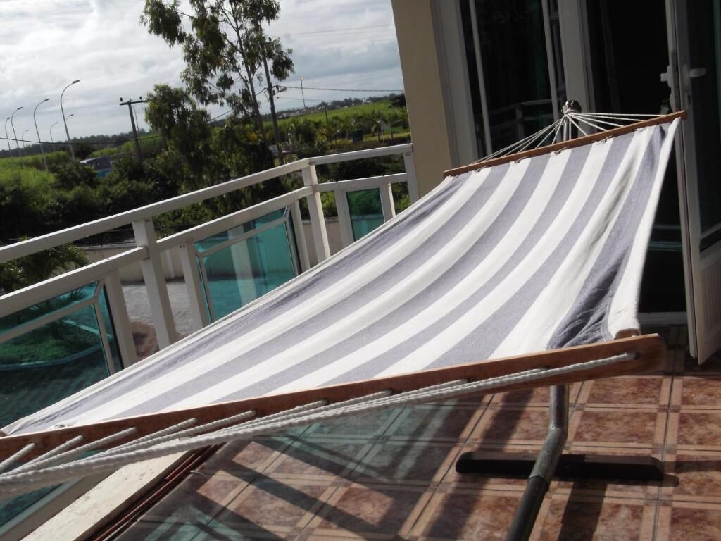 A hammock on a balcony with a view of greenery and a building in the background.