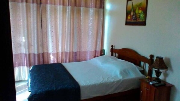 Un dormitorio con cama, mesita de noche, lámpara y un cuadro en la pared.