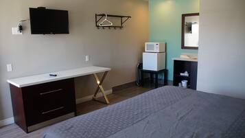 A bedroom with a bed, a desk, a microwave, and a small refrigerator.