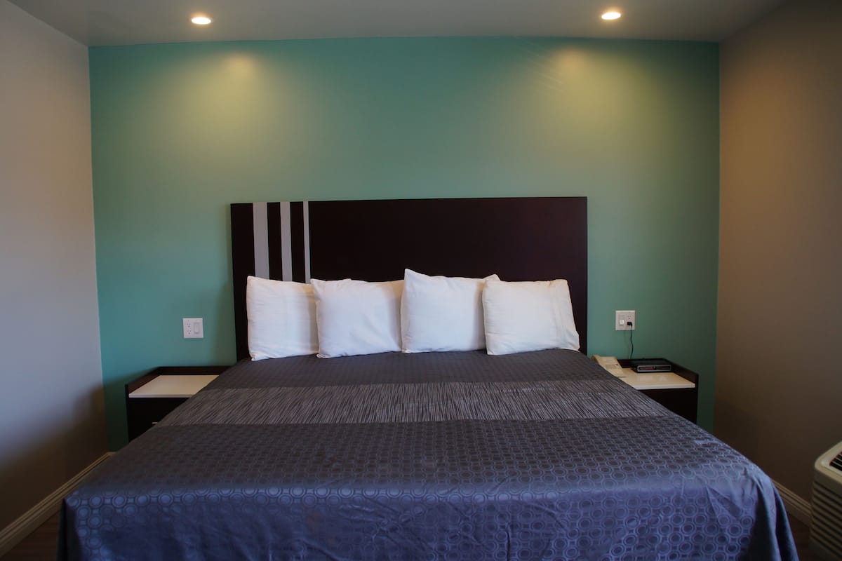 A neatly made bed with a dark blue bedspread and white pillows, a black headboard, and two bedside tables with a small lamp on each.