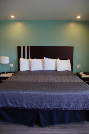 A neatly made bed with a dark headboard and white pillows, a bedside lamp, and a nightstand with a phone. - Beach Inn Motel (Long Beach)