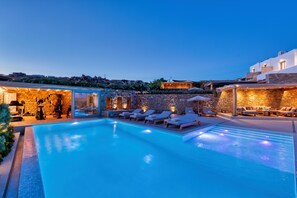 A swimming pool with lounge chairs and a spa area, surrounded by stone walls and a view of the hillside.
