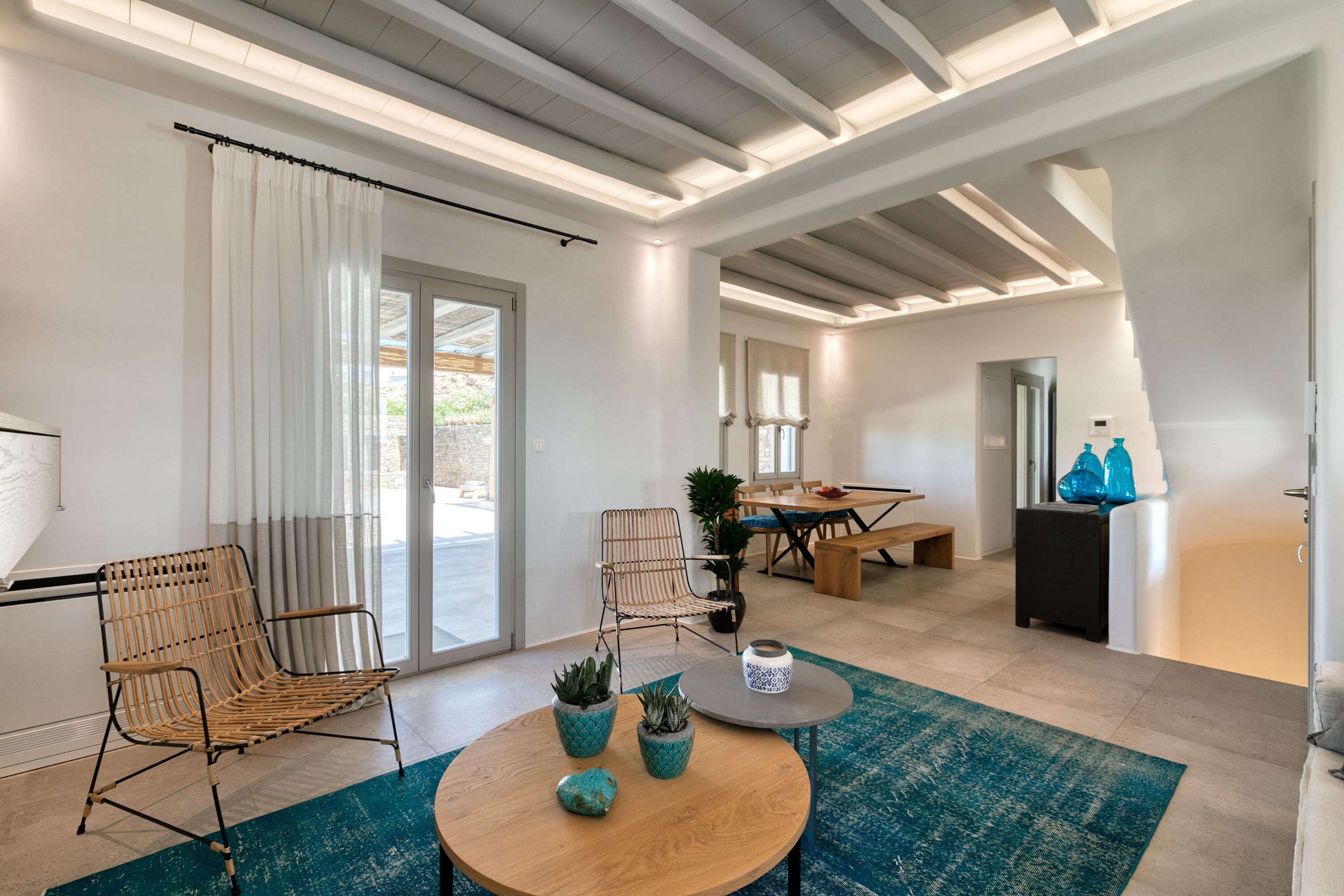 A modern living room with a wooden coffee table, two wicker chairs, and a dining area with a table and chairs.