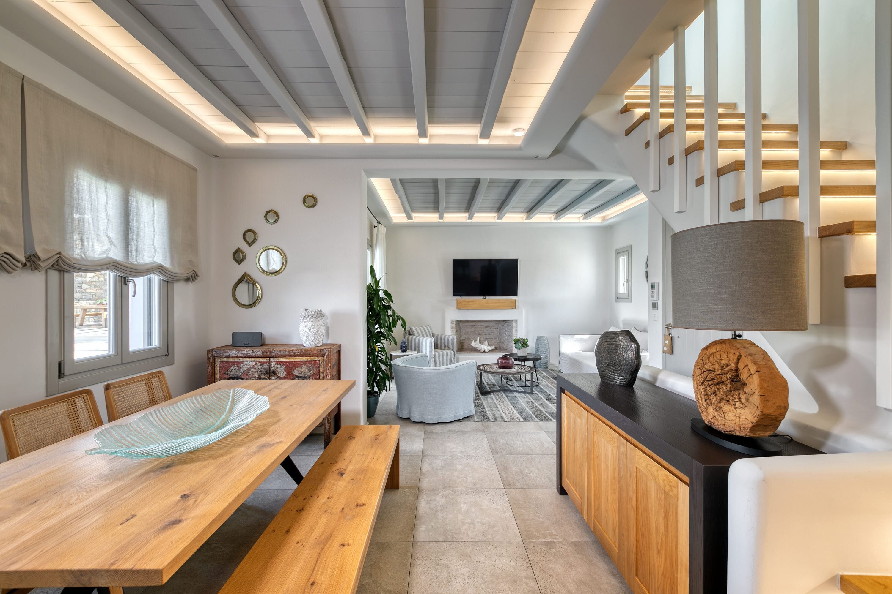 Uma sala de estar moderna com uma mesa de jantar de madeira, um sofá e uma TV na parede.