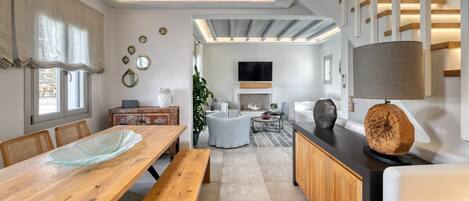 Uma sala de estar moderna com uma mesa de jantar de madeira, um sofá e uma TV na parede.