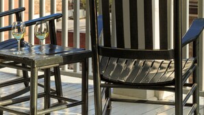 A balcony with a chair and table, a view of a church spire, and a building with a red facade. - The Inn on West Liberty (Savannah)