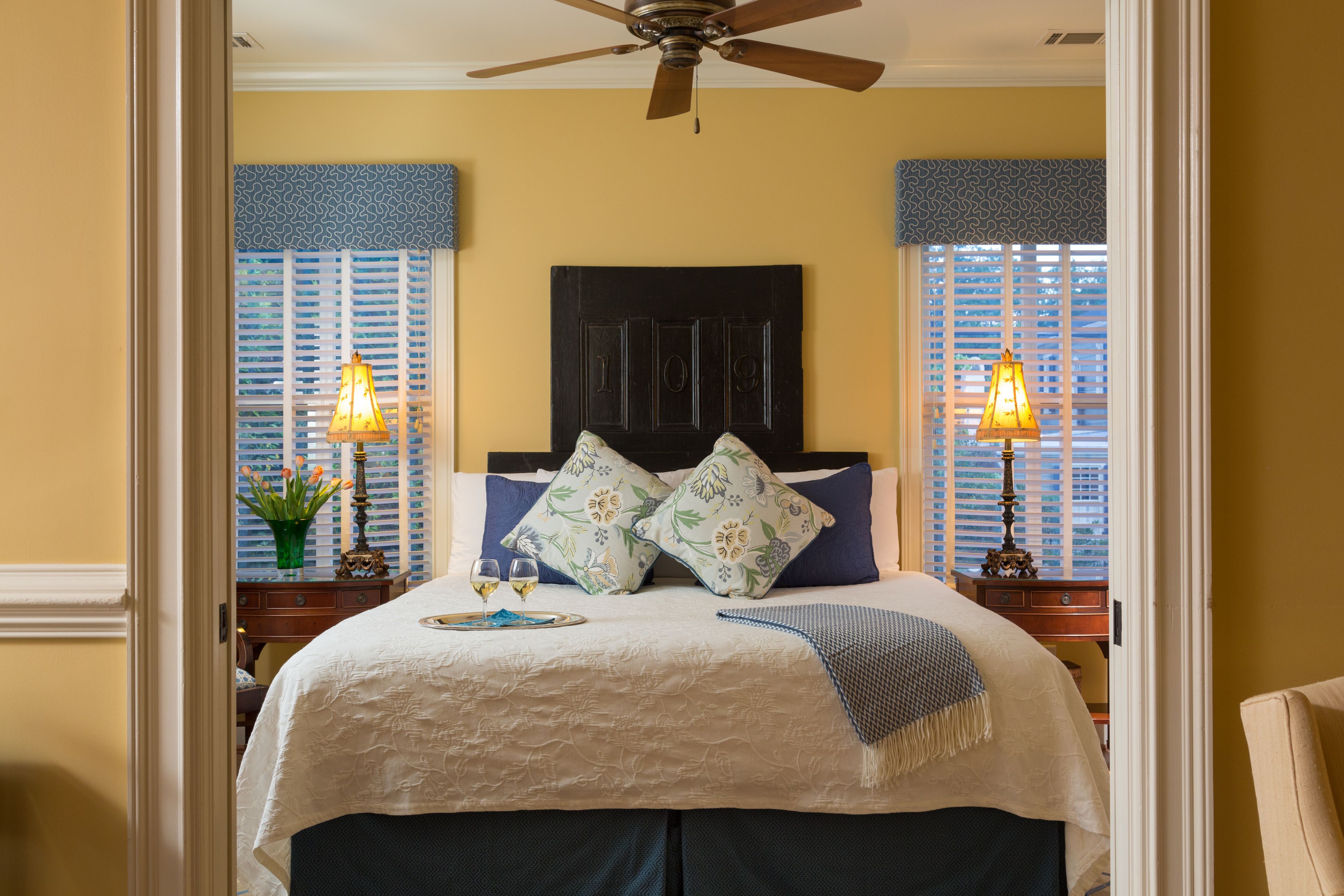 A bedroom with a bed, two bedside tables, a ceiling fan, and a window with blinds.