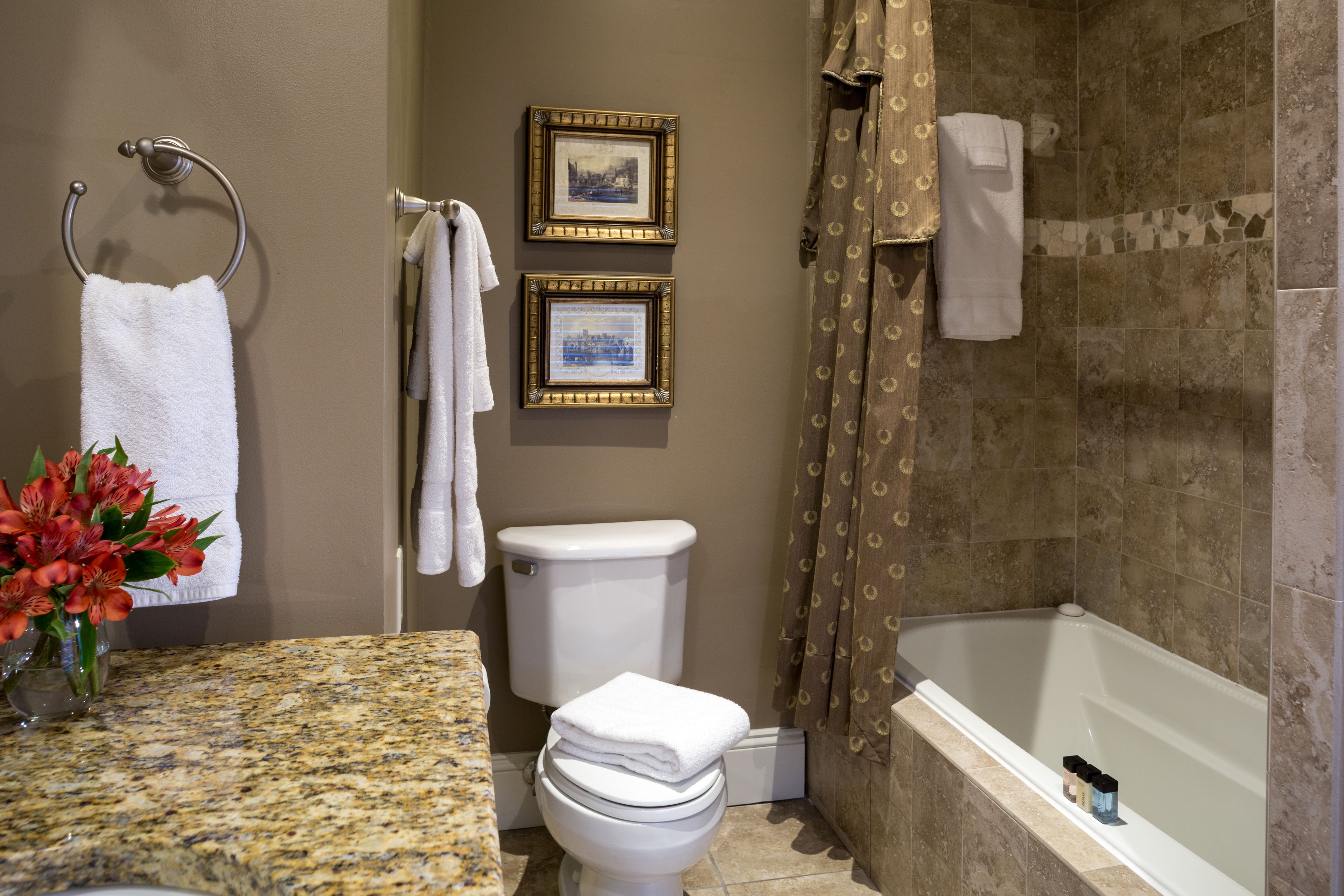 A bathroom with a toilet, sink, and bathtub. There are two framed pictures on the wall, a towel rack, and a vase with flowers on the sink counter.