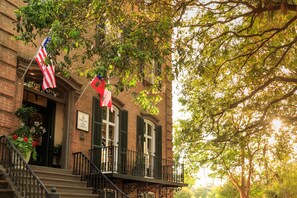 A historic building with a brick facade, a balcony with wrought iron railings, and American flags. - The Inn on West Liberty (Savannah)