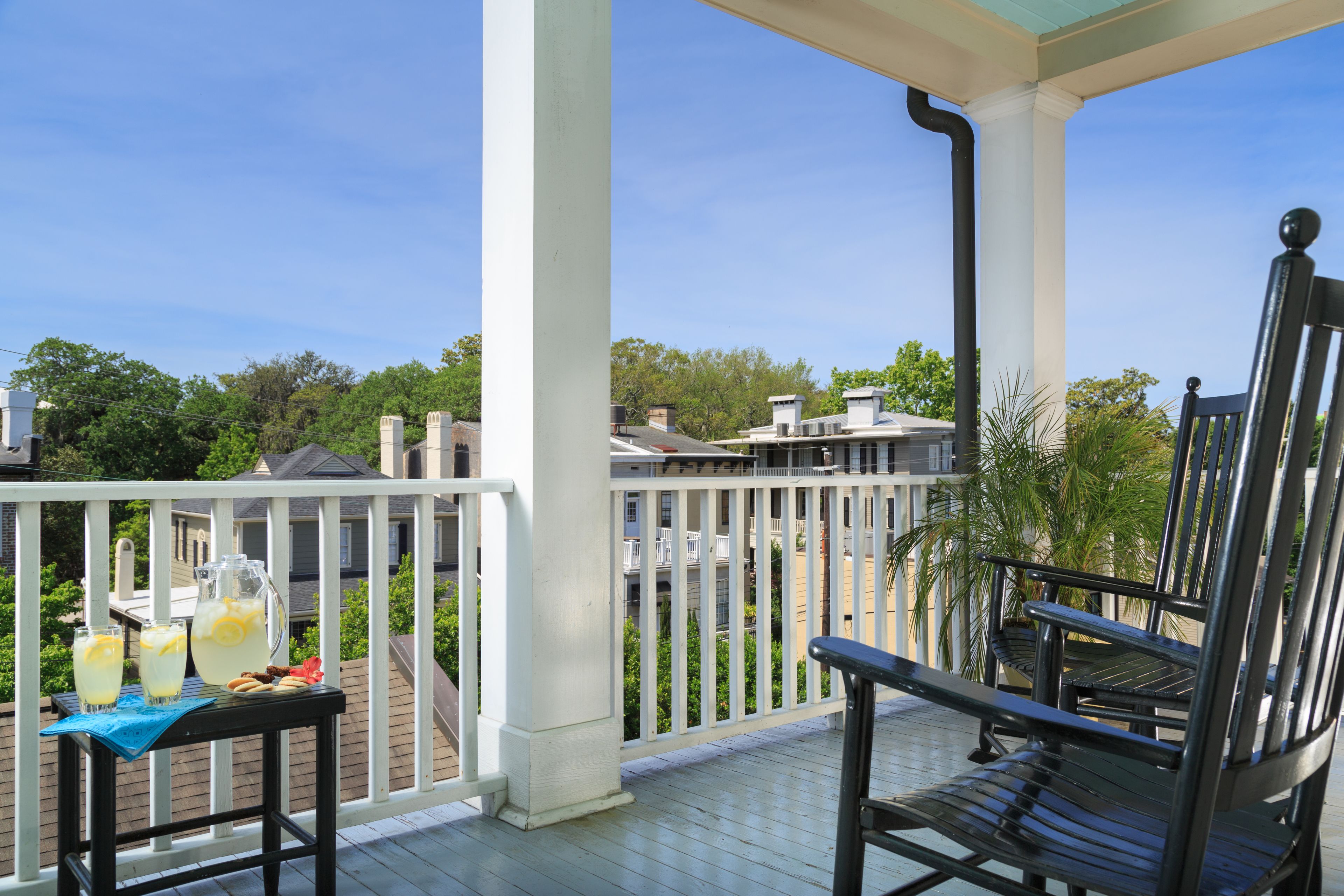 Un balcon avec une balustrade blanche, une chaise en métal noir et une table sur laquelle se trouvent une carafe et des verres.