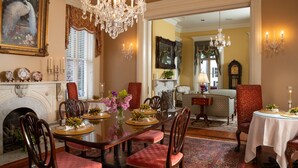 A dining room with a large table, chairs, chandeliers, and a fireplace. - The Inn on West Liberty (Savannah)