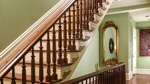 A wooden staircase with ornate balusters, a mirror with a gold frame, and a patterned tapestry on the wall. - The Inn on West Liberty (Savannah)