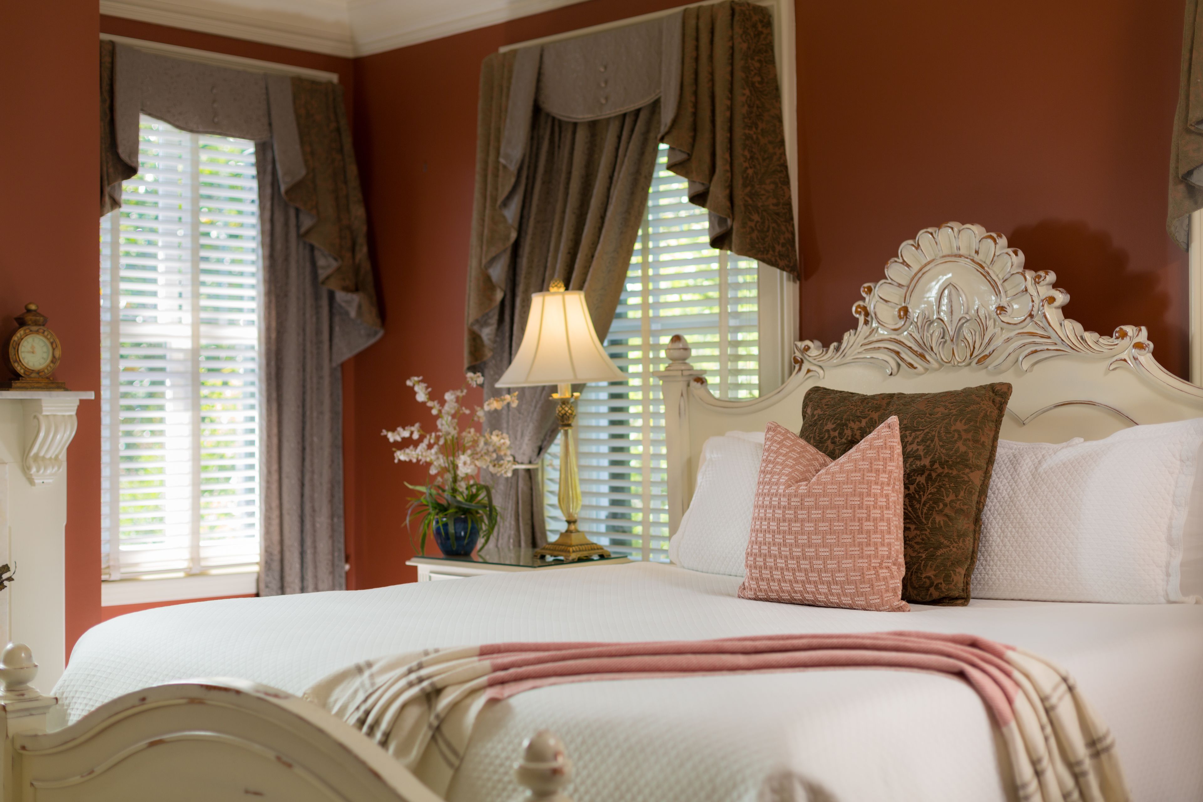 A neatly made bed with a white headboard, a bedside lamp, and a window with curtains.