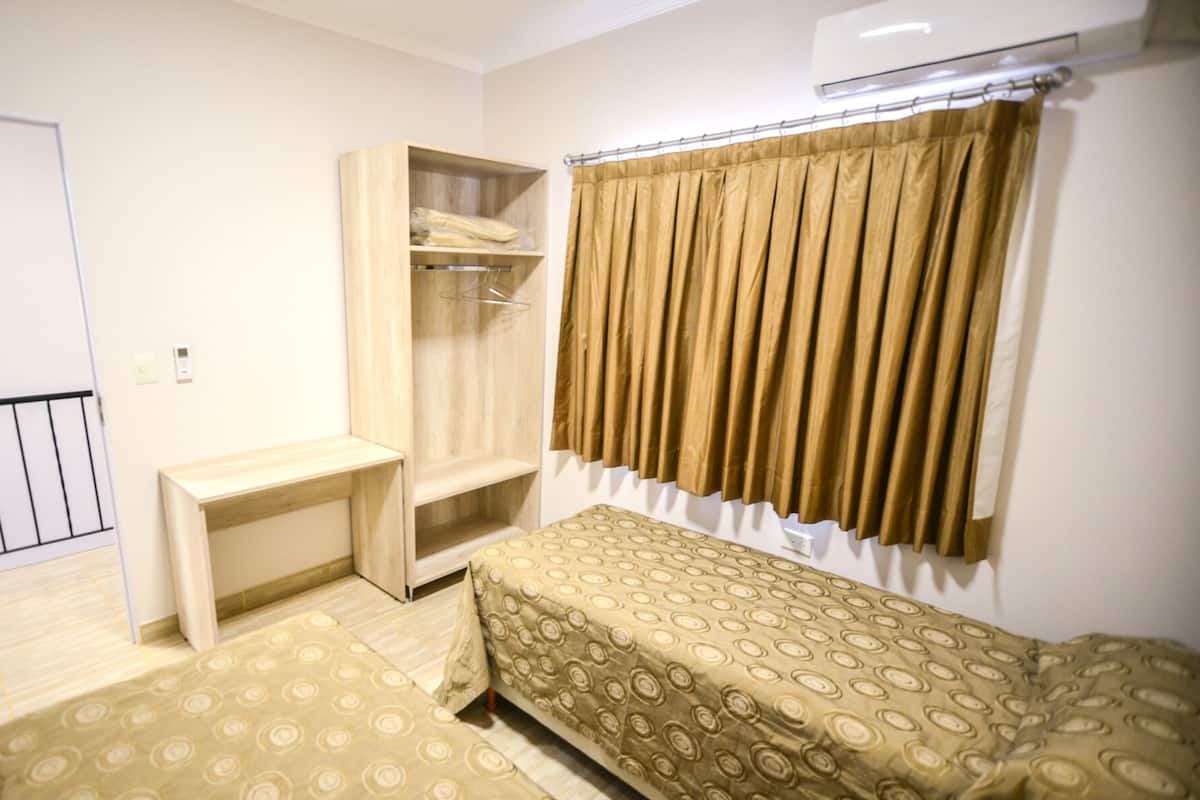 Ein kleines, ordentlich eingerichtetes Schlafzimmer mit einem Bett, einem Nachttisch, einem Kleiderschrank und einem Fenster mit Vorhängen.