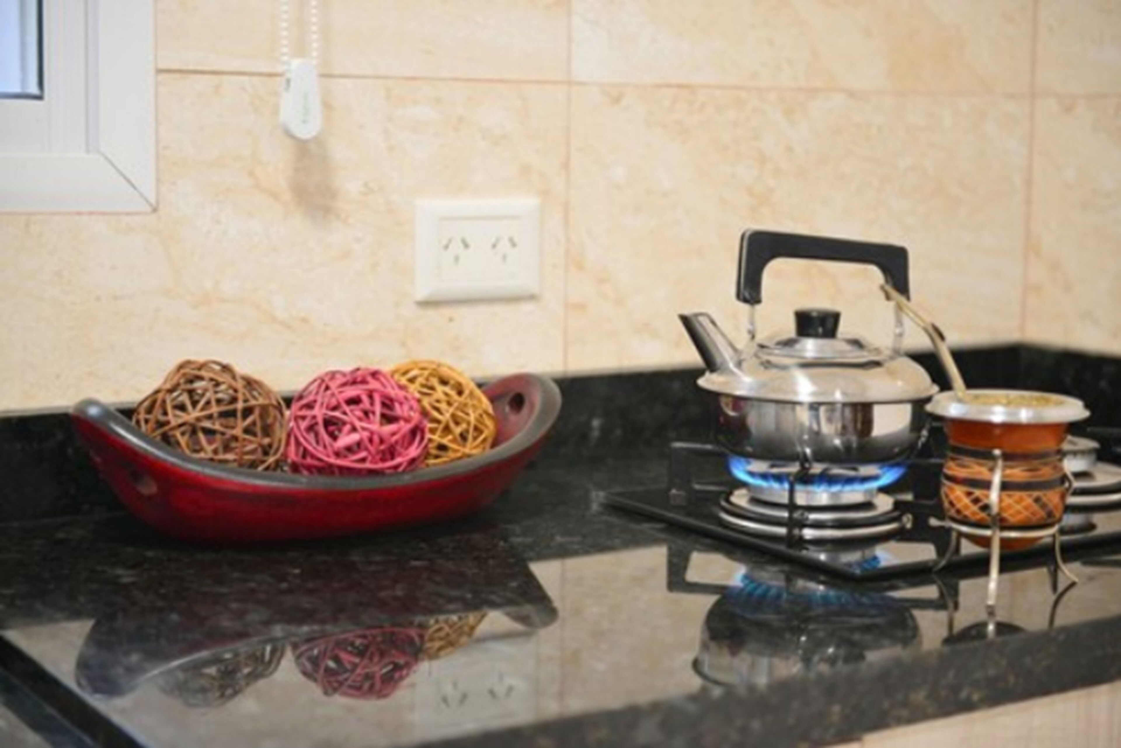A kitchen with a red bowl containing two balls of string, a gas stove with a pot, and a small burner.