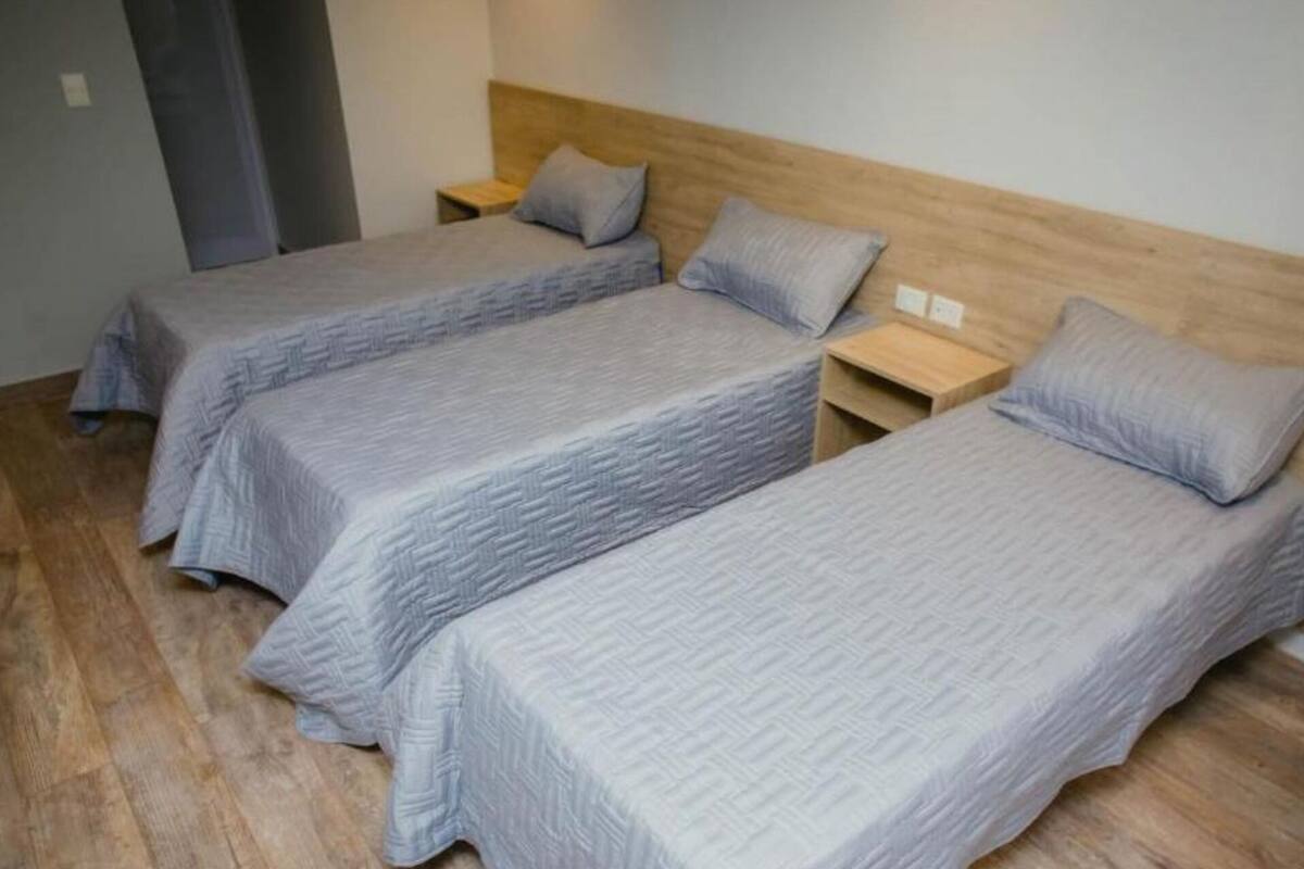 Drei Einzelbetten mit Holz-Kopfteilen und passenden Kissen, in einer Reihe angeordnet, mit dazugehörigen Nachttischen.