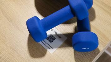 Un par de mancuernas azules con etiqueta de peso y un código QR sobre una superficie de madera.