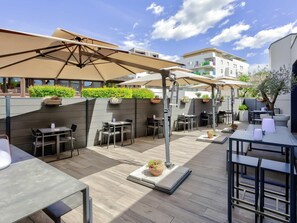 Une terrasse extérieure avec des tables et des chaises, des parasols et des plantes en pot.