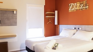 Una habitación de hotel con cama, cabecera de madera, pared blanca, puerta y ventana.