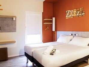 Ein Hotelzimmer mit Bett, Holz-Kopfteil, weißer Wand, einer Tür und einem Fenster.